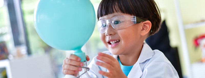 Sininen ilmapallo ja tieteellistä koetta tekevä iloinen lapsi.