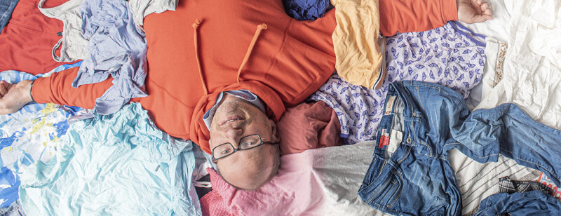 Petri Alava makaa selällään kierrätykseen menevien puhtaiden vaatteiden keskellä