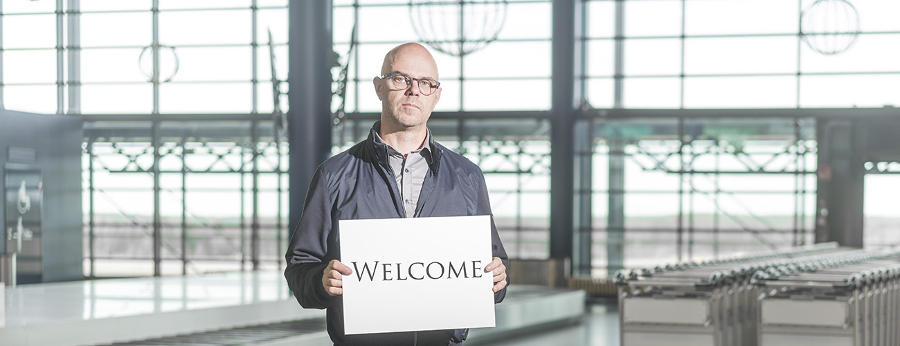 Harri Mällinen seisoo Rovaniemen lentoasemalla kädessään pahvinen kyltti, jossa lukee Welcome.