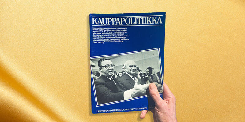 Käsi pitelee vuoden 1984 Kauppapolitiikka-julkaisua, jonka kannessa on valokuva poliittisista johtajista.