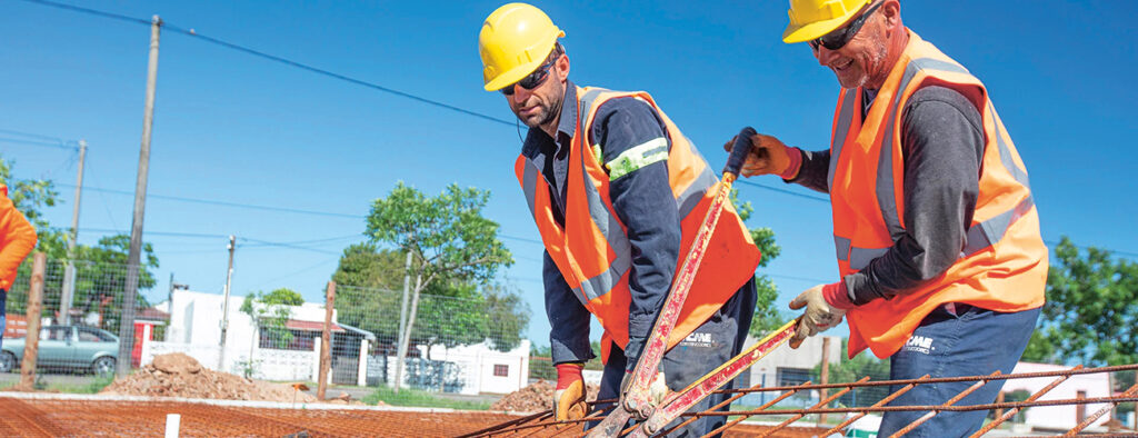 Kaksi työmiestä laikkaa raudoitusverkkoa oikeaan kokoon talon rakennustyömaalla Uruguayssa.