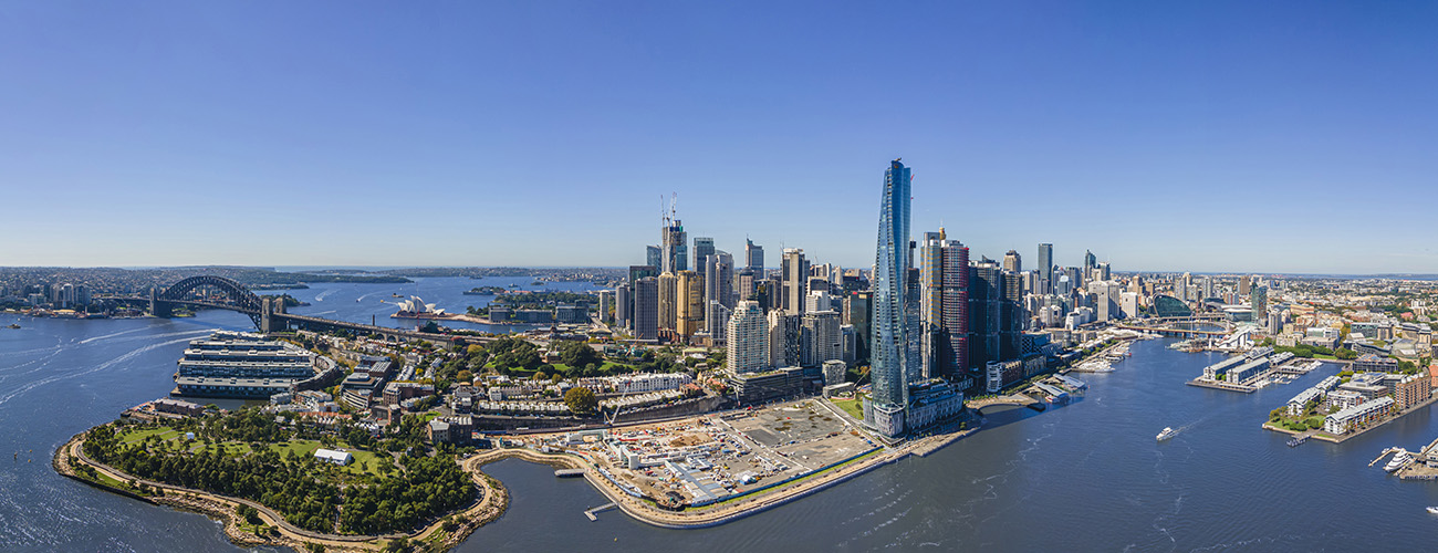 Laaja näkymä ilmasta päin aurinkoiseen Sydneyn keskustaan korkeine pilvenpiirtäjineen meren rannalla.