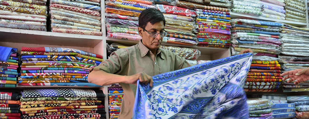 Mieshenkilö viikkaa kangaspakkaa intialaisessa kangaskaupassa